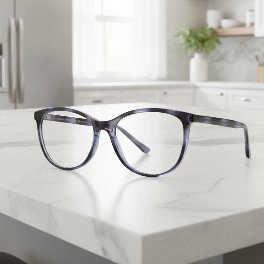 Exceptional Value collection eyeglasses featuring a translucent dark‑gray round acetate frame with thick rims, photographed on a marble countertop for Times Square Optical in Laredo, Texas.